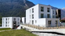 White apartment building, modern design, concrete driveway, green lawn, mountains in the background