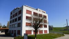 Building: multiple windows, red doors, signboard, grassy area, street