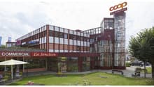 Commercial building, large glass windows, multiple floors, parking area, exterior seating, decorative signboard