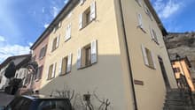 3 story building, beige walls, white windows, black car parked in front