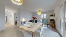 Dining room with a table, chairs, and a flower vase on the table. There is a lamp on the wall and a plant in the corner. The room has a sliding glass door leading to a balcony.