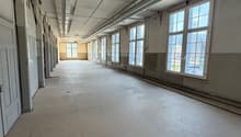 Empty room with white walls, ceiling, and floor, large windows, and doors on the left side