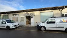 Single story building with a brown roof, white walls, several windows, and two vans parked in front