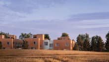 Modern architectural design, wooden exterior, multiple units, surrounded by trees and a field