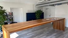Spacious office with hardwood-style flooring, large wooden desk, ceiling fan, and a balcony or terrace visible through the window.