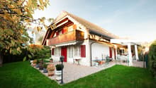white house, brown roof, red shutters, balcony, patio, garden, lawn, trees