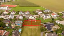 Houses in a residential area, with fields and a tennis court in the background. A swimming pool is visible in the bottom left corner.