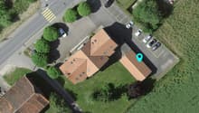 A two story house with brown roof, parking area with several cars parked, trees in the area
