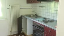 Compact kitchen with brown cabinets, white tile backsplash, stove, sink, and hexagonal tile flooring