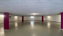 Large open space with concrete floor, white walls, and red columns. The room appears to be a basement or garage area with overhead lighting.
