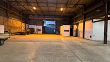 large warehouse with high ceilings, open space, brick walls, metal racks, 2 white doors, a truck with trailer parked at the entrance, steel door at the end of the room