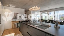 modern kitchen with large windows, wooden floor, large island with 2 sinks, chandelier, dining table, chairs