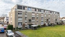 4 story apartment building, grey exterior, multiple windows, bicycles parked outside, green lawn in front