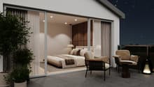 Spacious bedroom with large windows, sliding glass doors leading to a balcony or terrace, wooden accent wall, plush bedding, and comfortable seating area. The night sky is visible through the windows, creating a cozy and relaxing atmosphere.