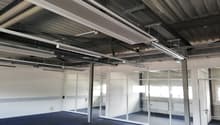 Large open space with office walls and glass doors, metal ceiling with overhead pipes and lighting