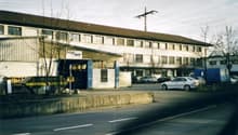 A building with several windows, parked cars in front, street light pole, road.
