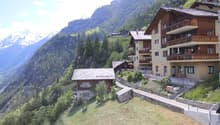 multiple wooden buildings, located on the slopes of a mountain, surrounded by greenery, offering a stunning panoramic view of the surrounding mountains