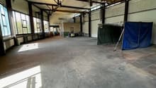 Large open space with concrete floor, exposed ceiling beams, and windows along the walls. The space appears to be a warehouse or industrial facility with some equipment and storage items visible.