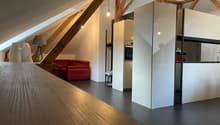 Exposed wooden beams, red couch, grey carpet, white kitchen, lamp, ceiling lamp, wooden table