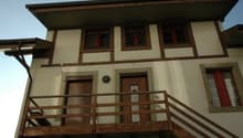 2 story house, beige and brown trim, wooden balcony, wooden doors, windows with red frames