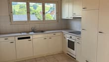 modern kitchen with white cabinets, tiled floor, granite countertop, sink, oven, dishwasher, and large windows with a view of the outdoor landscape.
