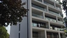 Multi-story apartment building with balconies, glass windows, and a modern, minimalist design.