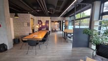 large open space with wood flooring, long wooden table, modern chairs, brick wall, bright windows, office setting
