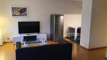 Living room with a sofa, glass table, white furniture, television, refrigerator, and a picture frame mounted on the wall.