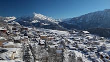 Mountain village in winter, snow covered houses, pine trees, and mountains in the background