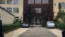 Three story building, brick walls, glass windows, two cars parked in front, gravel driveway