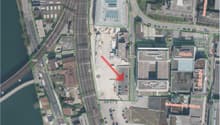 This image shows an aerial view of a commercial and industrial area. The main features visible include a large school building labeled 'Fachhochschule FHNW', a parking lot, and several other commercial and industrial buildings in the surrounding area.