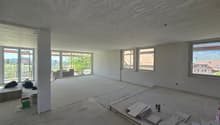 Empty room with white walls, concrete floor, large windows, construction materials on the floor