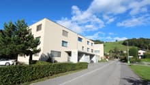 3 story building, parking area in front, white exterior, window grills, located in a green area