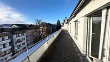 View of a roof terrace with paved floor, metal railings, and a clear view of the skyline.