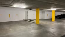 underground parking lot, white walls, yellow pillars, numbered parking spots, a black car parked in spot 27