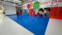 Large indoor retail space with blue flooring, various sports and outdoor equipment brands displayed on the walls, and signs advertising sales and discounts.