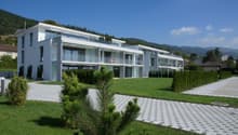 Modern two-story apartment building, white exterior, glass balconies, landscaped front yard