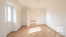 Empty room with wooden parquet flooring, white walls, two windows, and an open door leading to another room.