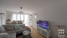 modern living room with gray couch, glass table, TV, wooden floor, white walls, dining table, chairs, plants