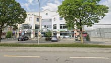Buildings with restaurants, 2 cars parked, trees in front, road with lane markings