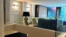 Spacious living room with modern decor, including a fireplace, arched windows, and a large sofa. The room has a mix of contemporary and traditional elements, with a stone accent wall and recessed lighting.
