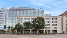 Modern office building with glass facade, multiple floors, entrance with glass doors, street with cars and bicycles