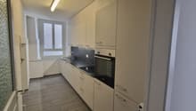 modern kitchen, white cabinets, tiled floor, black countertops, built-in oven, sink, dishwasher, washing machine