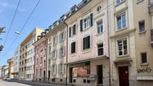 An outdoor view of a row of buildings with windows and doors on a street with parked cars, street lights, and wires