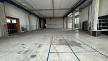 large room with high ceiling, blue lines on the floor, concrete walls, some equipment and furniture