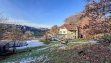 Detached house with red roof, glass windows, snow on the ground, trees, mountains, clear blue sky