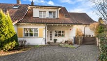 Detached 2-story house, red tiled roof, white walls, yellow shutters, a driveway, fenced front yard, several plants in front