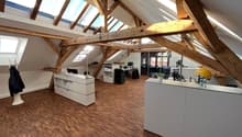 wooden beams, wooden floor, white walls, office desks, monitors, lamps, potted plants