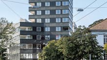 Apartment building with balconies, modern design, multiple windows, grey exterior, sign reading 'Baren Tour'.