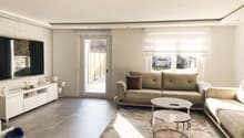 modern living room with white walls, gray floor, two couches, coffee table, TV, white entertainment center, glass door